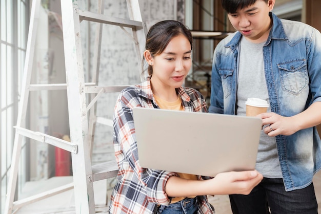 Gratis Foto twee aziatische mannelijke en vrouwelijke aannemers raadplegen en onderzoeken bij renovatie van het huis met laptop en papiertekening aziatische ingenieur en ontwerper leggen uit en bespreken op bouwplaats