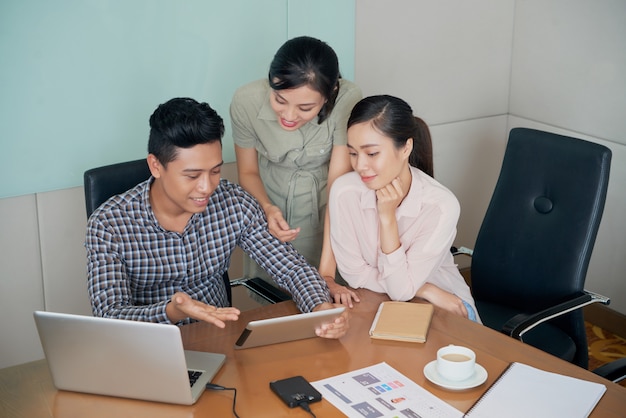 Gratis Foto vrolijke aziatische collega's die en bureau rondhangen zitten en tablet samen bekijken