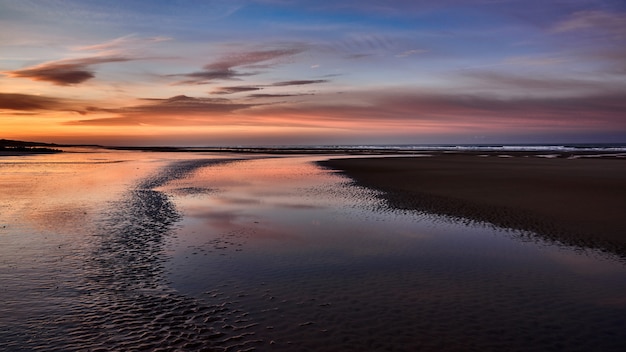 Gratis foto wide shot van de prachtige kust van de zee met de verbazingwekkende bewolkte hemel tijdens gouden uur