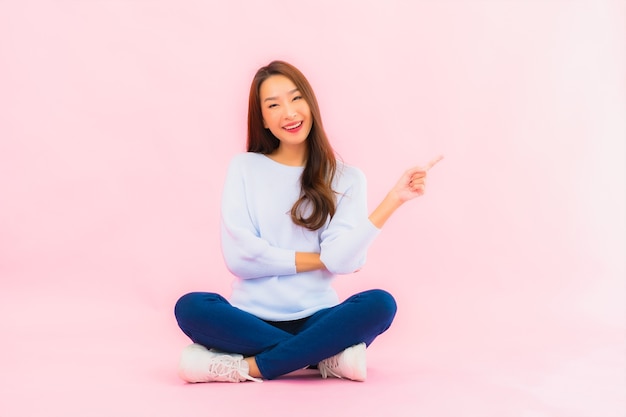 Gratis Foto zit de portret mooie jonge aziatische vrouw op vloer met roze kleur geïsoleerde muur