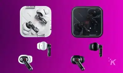 Two pairs of wireless earbuds with transparent design, one set in white and the other in black, displayed both in their open charging cases and separately outside the cases, against a purple background.