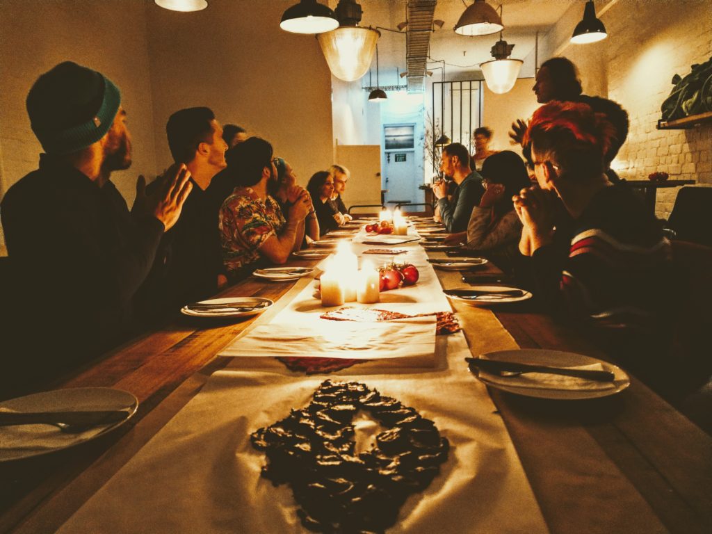 A group of people sitting around a long wooden table with plates in front of them