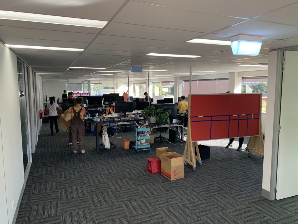 An office scene featuring people carrying items, desks, and boards