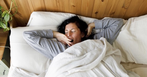 Woman with eyes closed yawning in bed at home