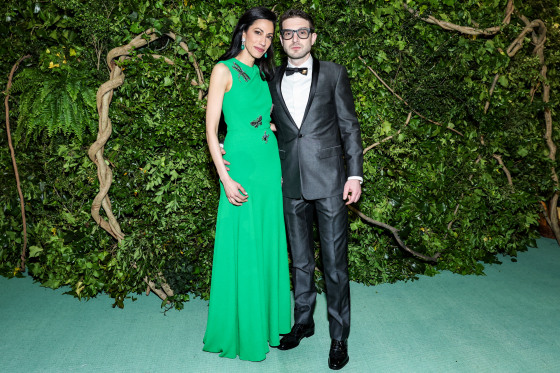 Huma Abedin and Alexander Soros pose together on the green carpet in front of foliage