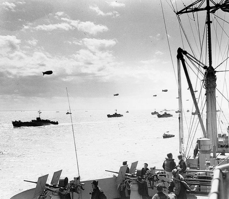 A convoy of infantry transport ships head toward the Normandy beaches on June 6, 1944, as seen from the USS Ancon. Barrage balloons, which defend against attack from loy-flying aircraft, float overhead.