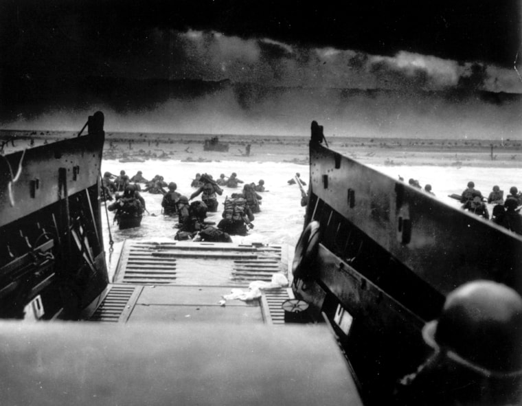 While under attack from heavy machine gun fire from the German coastal defense forces, American soldiers wade ashore off the ramp of a U.S. Coast Guard landing craft.