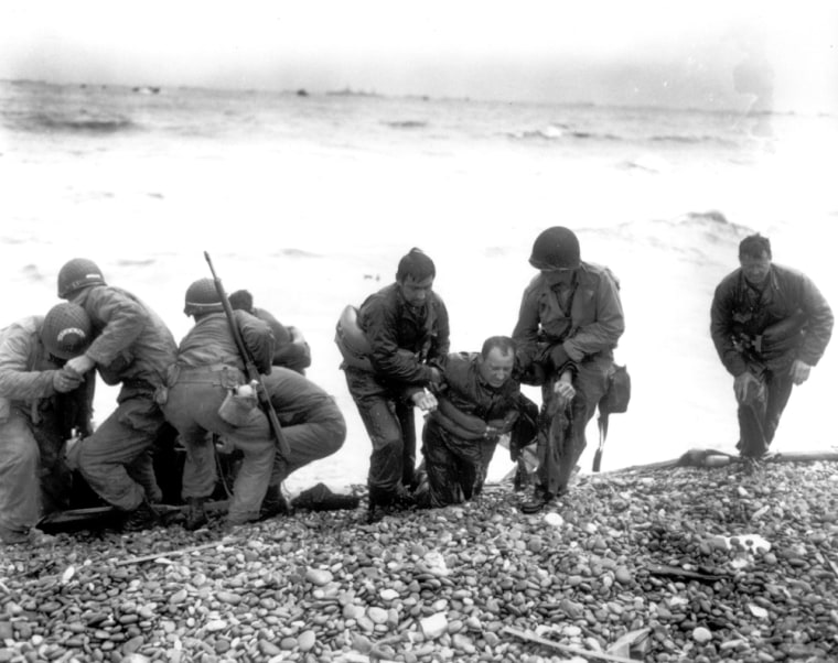 Members of an American landing unit help their exhausted comrades ashore. The men reached the zone code-named Utah Beach, near Sainte-Mere-Eglise, on a life raft, after their landing craft was hit and sunk by German coastal defenses.