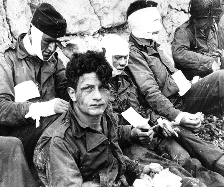 Army wounded are given cigarettes and food on Omaha Beach. The U.S. 1st Infantry Division suffered 2,500 casualties on the first day of the invasion.