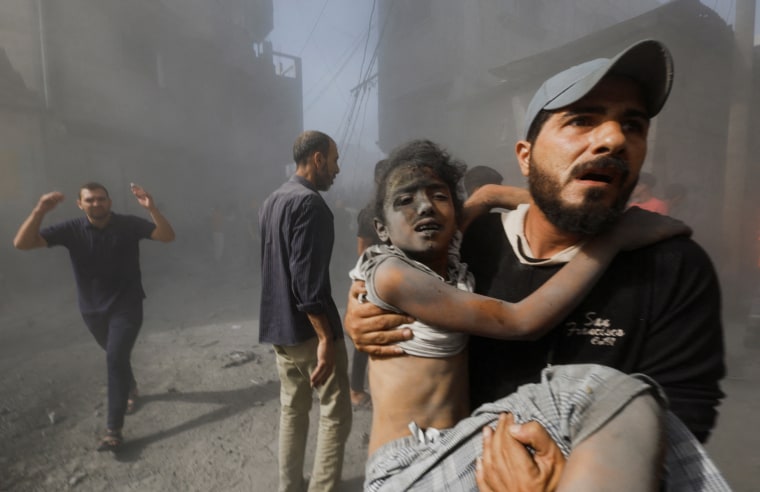 A Palestinian man carries a child casualty at the site of Israeli strikes on houses, in Khan Younis