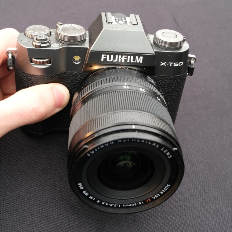 A hand holding the Fujifilm X-T50 camera over a table with a black cloth.