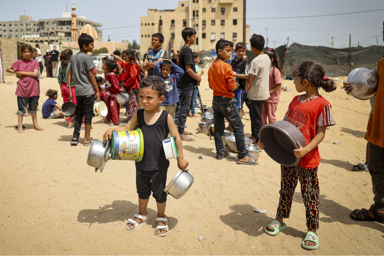 Displaced Palestinian children holding pans, line up to receive food in Rafah, Gaza