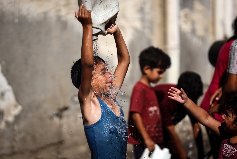 A displaced Palestinian boy is cooling himself with water.