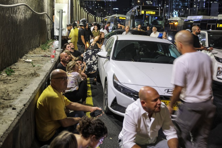 People take cover behind vehicles under a bridge in Tel Aviv.