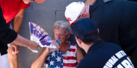 A woman drinks a bottle of water surrounded by people trying to help her 