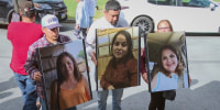 Three people hold large photo posters of their family members