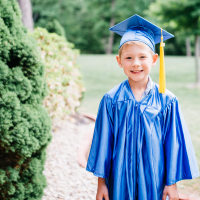 Portrait of happy boy in graduation gown standing at park