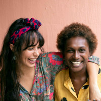 two young women friends laughing in front of pink wall