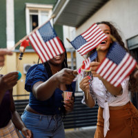 Candid shot of diverse group of joyful young people, friends, having fun, dancing and waving American flags while celebrating 4th of July on the balcony.