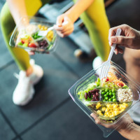 Two athletes eating salad after exercise at fitness gym.