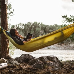 Young man reading book while lying down over hammock in forest