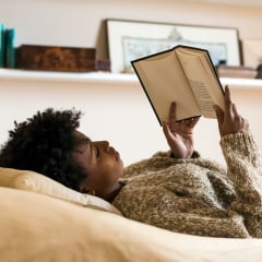 Young woman lying on bed reading a book.