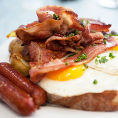 A closeup of eggs, bacon, ham, and sausage on top of toast