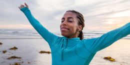 Celebration of Life. Beautiful woman if mixed race. Her arms raised up in the air. Her head is tilted back and eyes are close. She is in awe and smiling at the beauty of nature. Woman is expressing positivity, and feels grateful for life. She is very spiritual. Woman is at the beach with beautiful sunset in the background. 