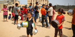 Displaced Palestinian children holding pans, line up to receive food in Rafah, Gaza