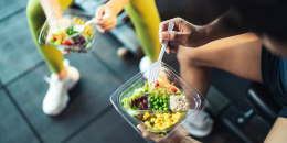 Two athletes eating salad after exercise at fitness gym.