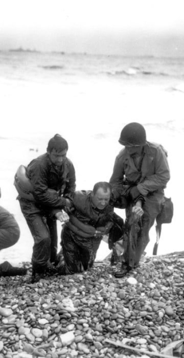 Members of an American landing unit help their exhausted comrades ashore. The men reached the zone code-named Utah Beach, near Sainte-Mere-Eglise, on a life raft, after their landing craft was hit and sunk by German coastal defenses.