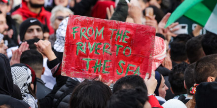 A crowd of protestors, including one holding up a sign that reads: "From the River to the Sea"