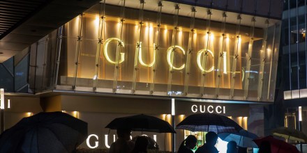 Pedestrians holding umbrellas walk past a Gucci luxury goods store, operated by Kering SA, at night in the Lujiazui district of Shanghai, China.