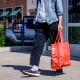 A shopper exits an Aldi supermarket carrying a red shopping bag