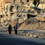 Image: Displaced Palestinians walk past destroyed buildings