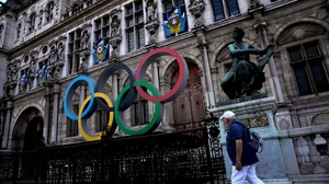 (AP Photo/Christophe Ena, File) : A man walks past the Olympic rings in front of the Paris City Hall one year until the Paris 2024 Olympic Games opening ceremony, Wednesday, July 26, 2023. 