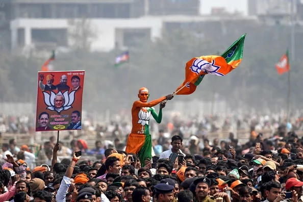 A Bharatiya Janata Party (BJP) supporter waves a flag among the crowd of other supporters listening to Prime Minister Narendra Modi at a rally - Getty Images