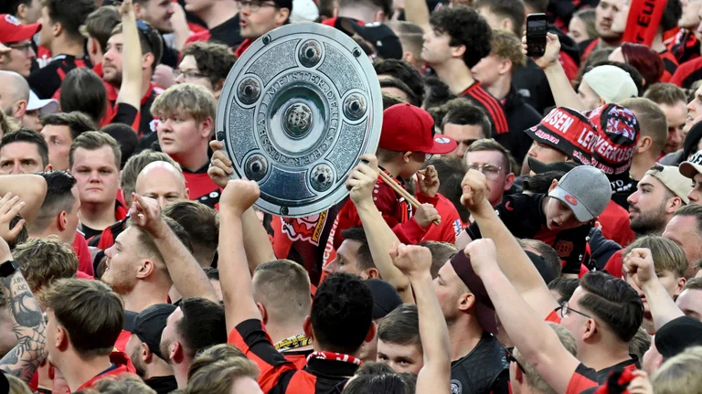 Leverkusen's fans raise a mock champions trophy as they celebrate winning the German championship on the pitch after the Bundesliga soccer match between Bayer Leverkusen and Werder Bremen at the BayArena in Leverkusen, Germany, Sunday, April 14, 2024.  - (Federico Gambarini/dpa via AP)
