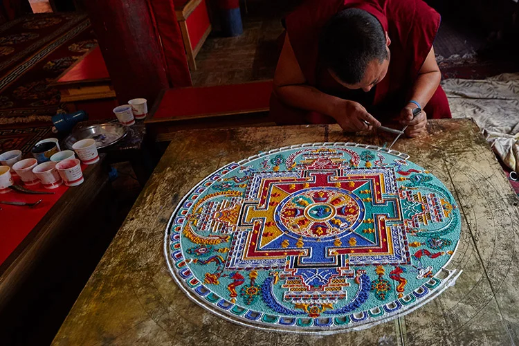 A monk painting a vibrant mandala on a table, showcasing intricate patterns and rich colors.