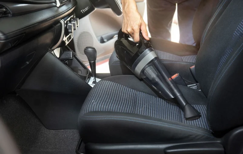 A hand with a car vacuum cleaner, cleaning the first seat