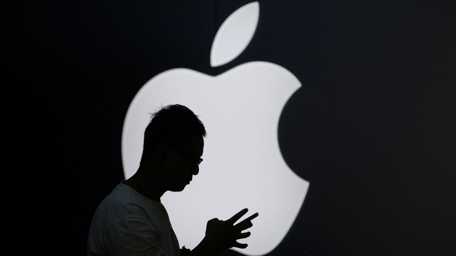 A man check his phone near an Apple logo outside its store in Shanghai, China September 13, 2023. REUTERS/Aly Song