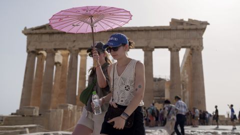 Tourists with an umbrella walk in front of the Parthenon at the ancient Acropolis in central Athens, Wednesday, June 12, 2024. The ancient site was closed to the public for five hours due to a heat wave that pushed temperatures to 39 degrees Celsius (102 Fahrenheit) in the capital and even higher in parts of central Greece. (AP Photo/Petros Giannakouris)