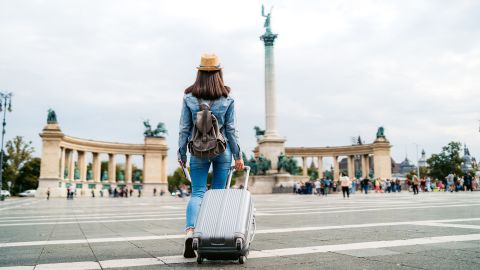 Young caucasian slim tourist woman visiting Budapest. Walking over Heroes' Square with luggage and map.