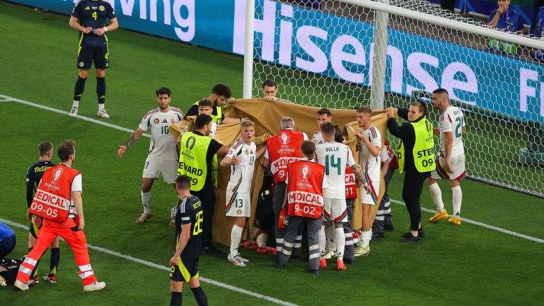 Players and stewards hold sheets to shield Barnabás Varga while he receives medical treatment.