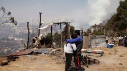 TOPSHOT - A couple embraces as smoke rises from a bushfire on a hill in Quito on September 25, 2024. Firefighters and helicopters were battling five forest fires Wednesday on the outskirts of Quito that have left six people injured and led to the evacuation of over 100 families. (Photo by Galo Paguay / AFP) (Photo by GALO PAGUAY/AFP via Getty Images)