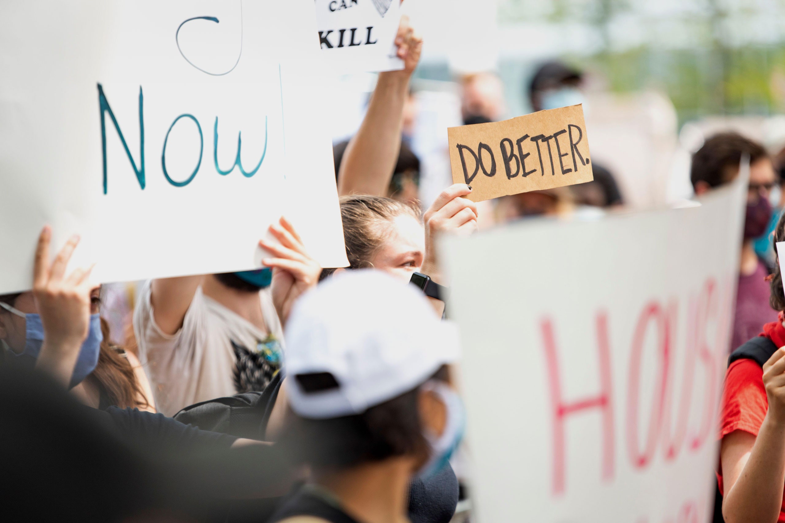 A woman holds a sign reading do better among a crowd of people