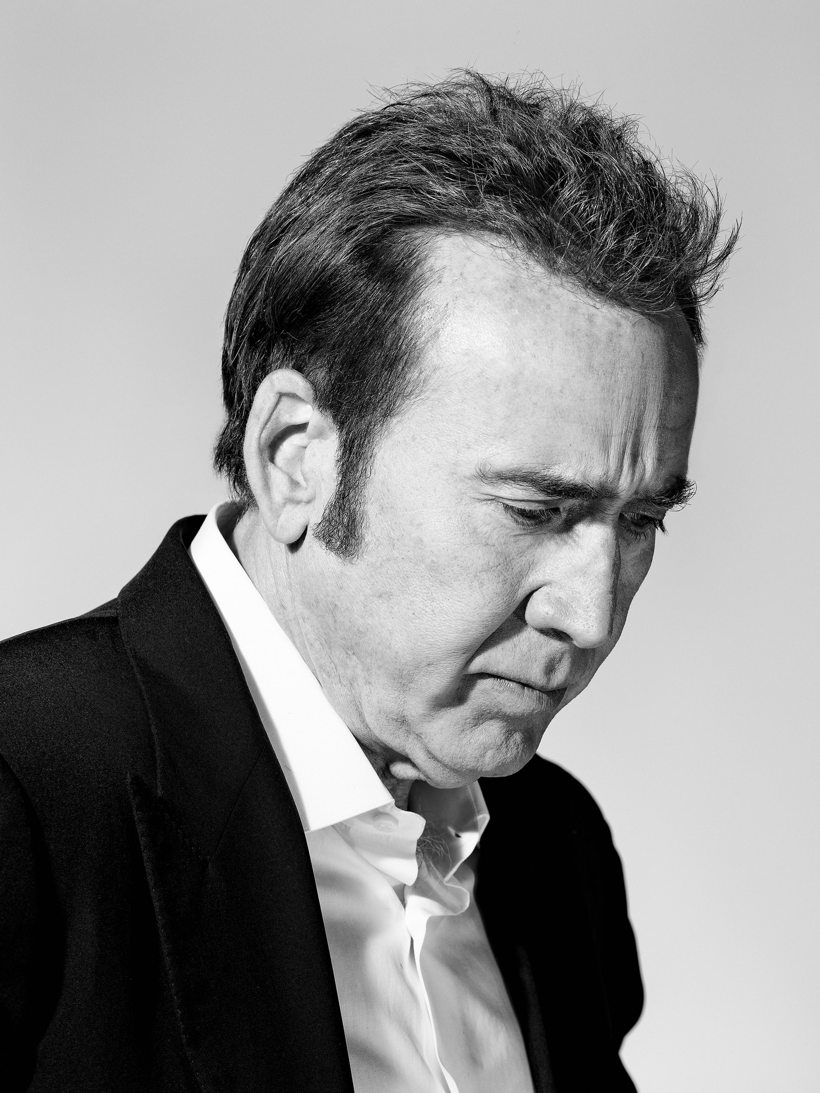 Black and white portrait of Nicolas Cage. Cage is looking down and wearing a black blazer with a white shirt.