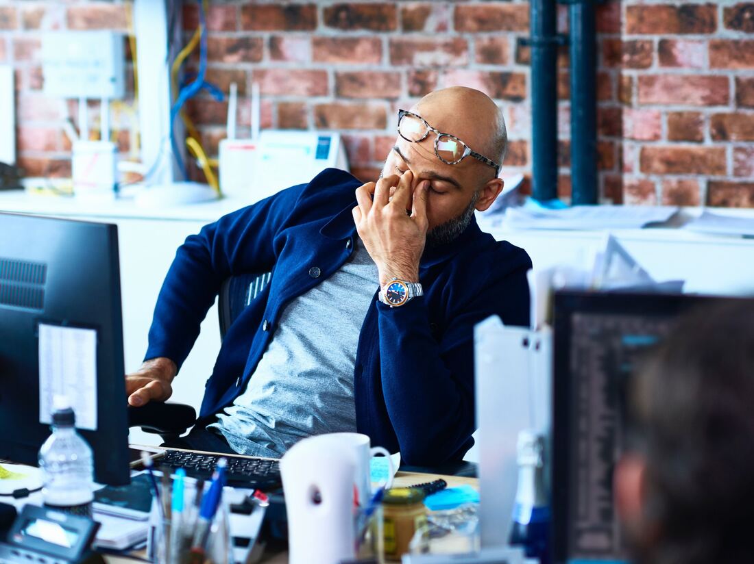 A tired man sits at a desk in a modern office.