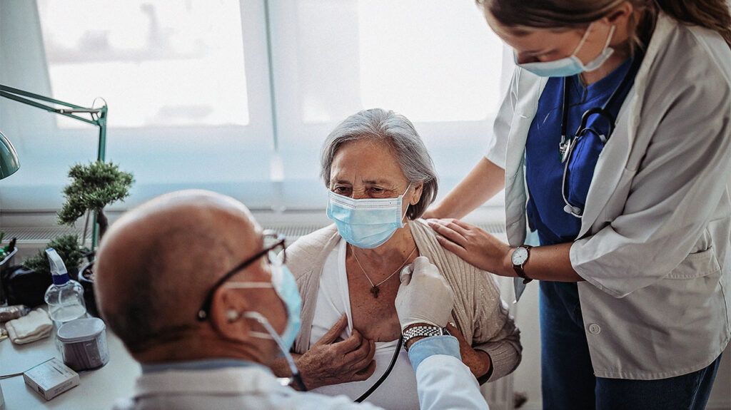 An older woman in hospital undergoing a physical examination from a doctor due to heart inflammation after COVID-19.