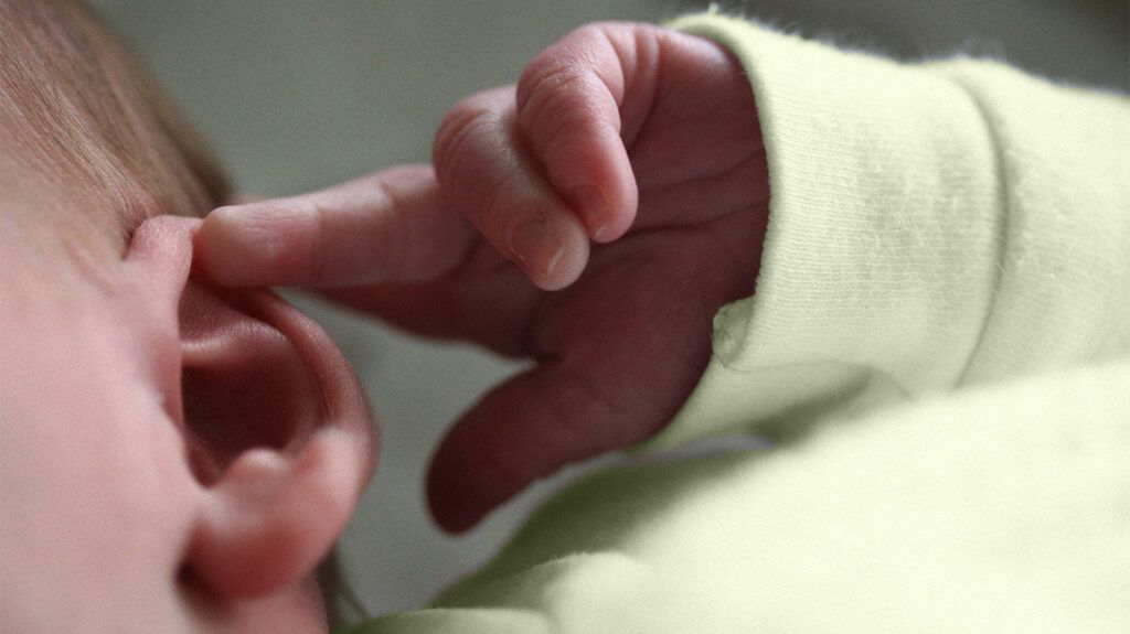 Infant touching their ear with their finger